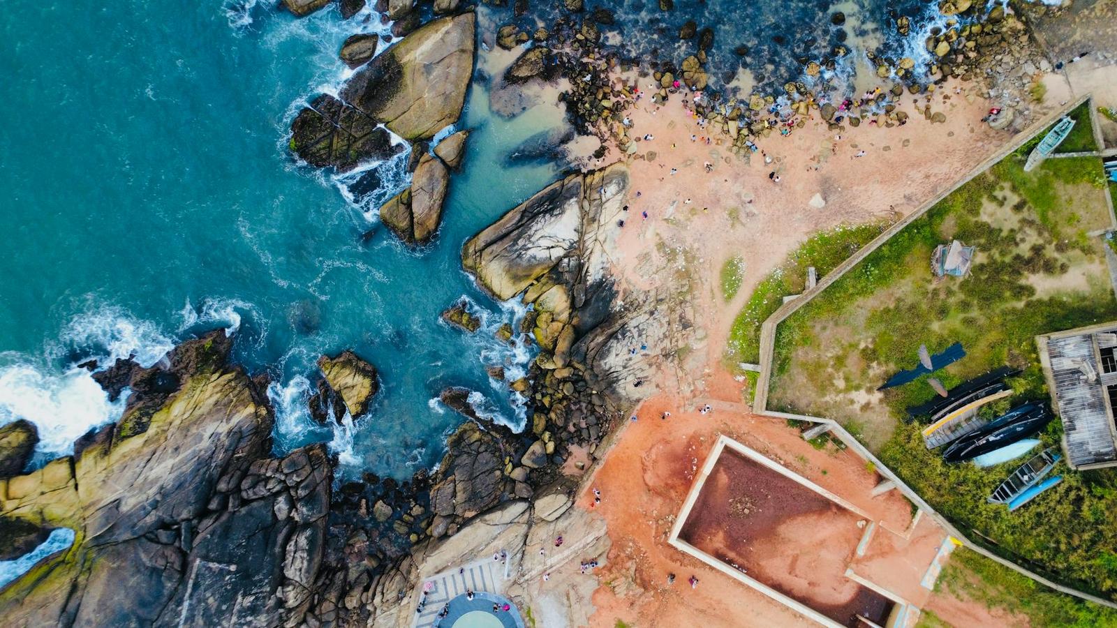 Aerial view of rocky turquoise coastline beside a sandy cove