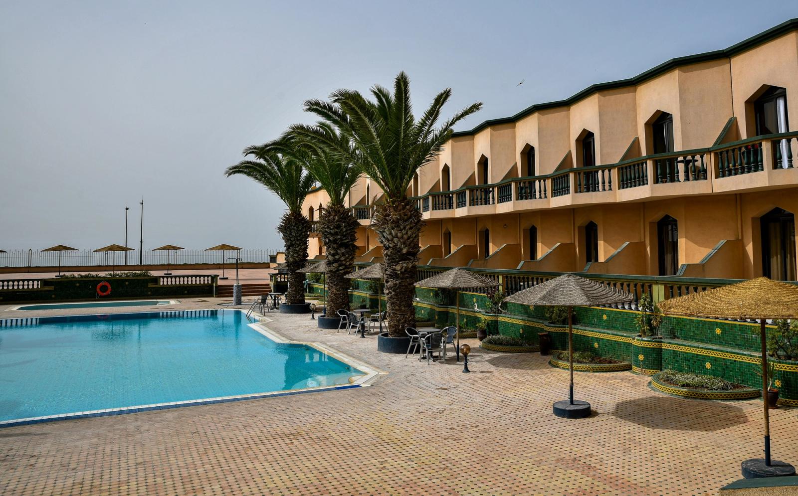 Resort with pool, palm trees, and hotel building A summer view of the courtyard at Hôtel Atlantique Panorama in Safi, Morocco, featuring a large blue swimming pool, rows of palm trees, sun umbrellas, 
