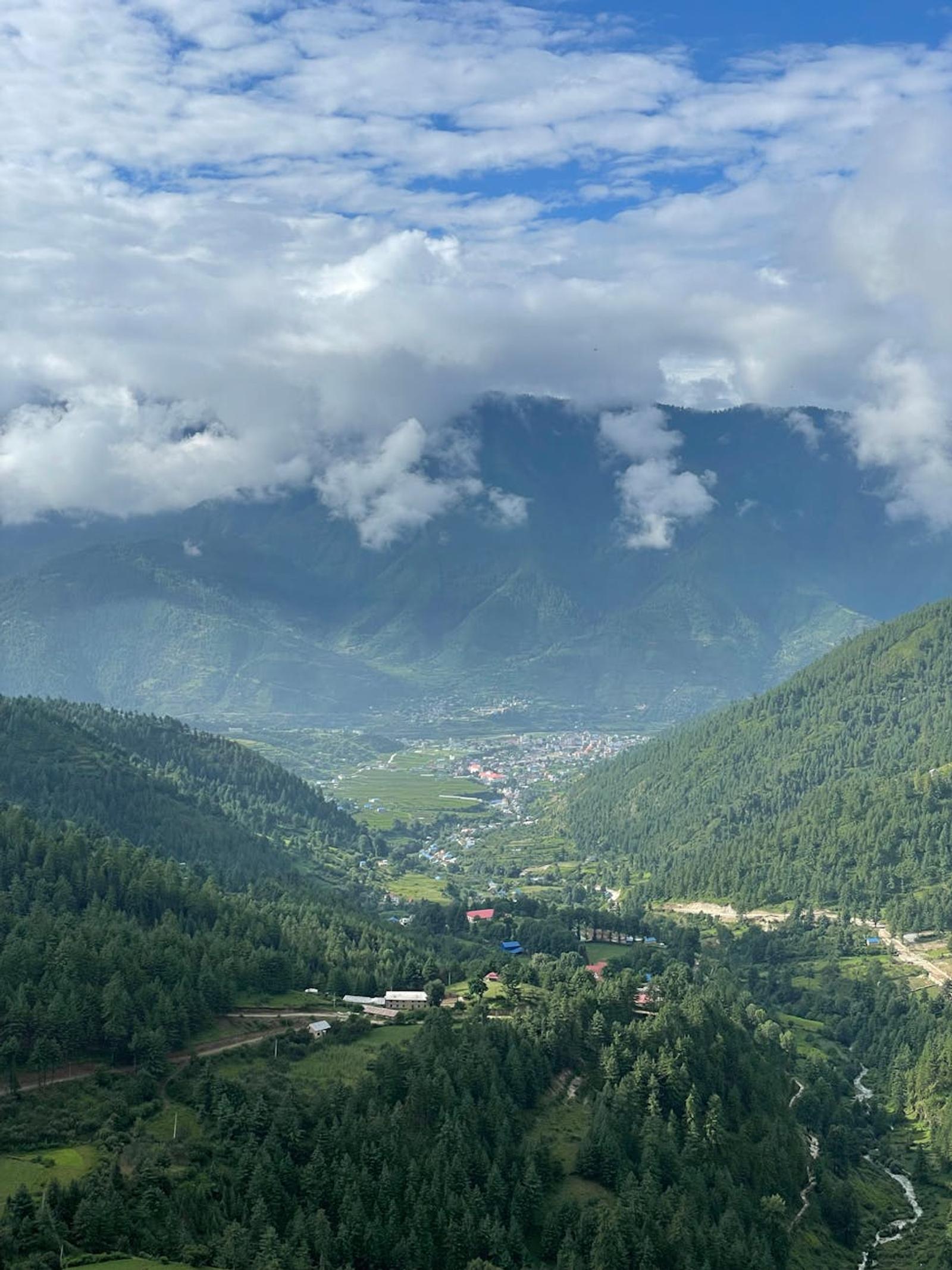 Scenic aerial view of a lush green valley with mountains and clouds under a bright sky