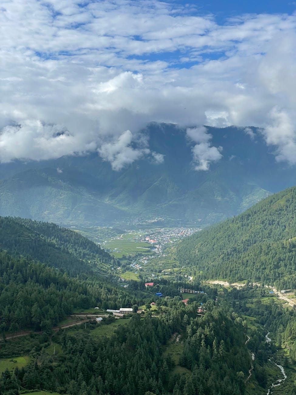 Scenic aerial view of a lush green valley with mountains and clouds under a bright sky
