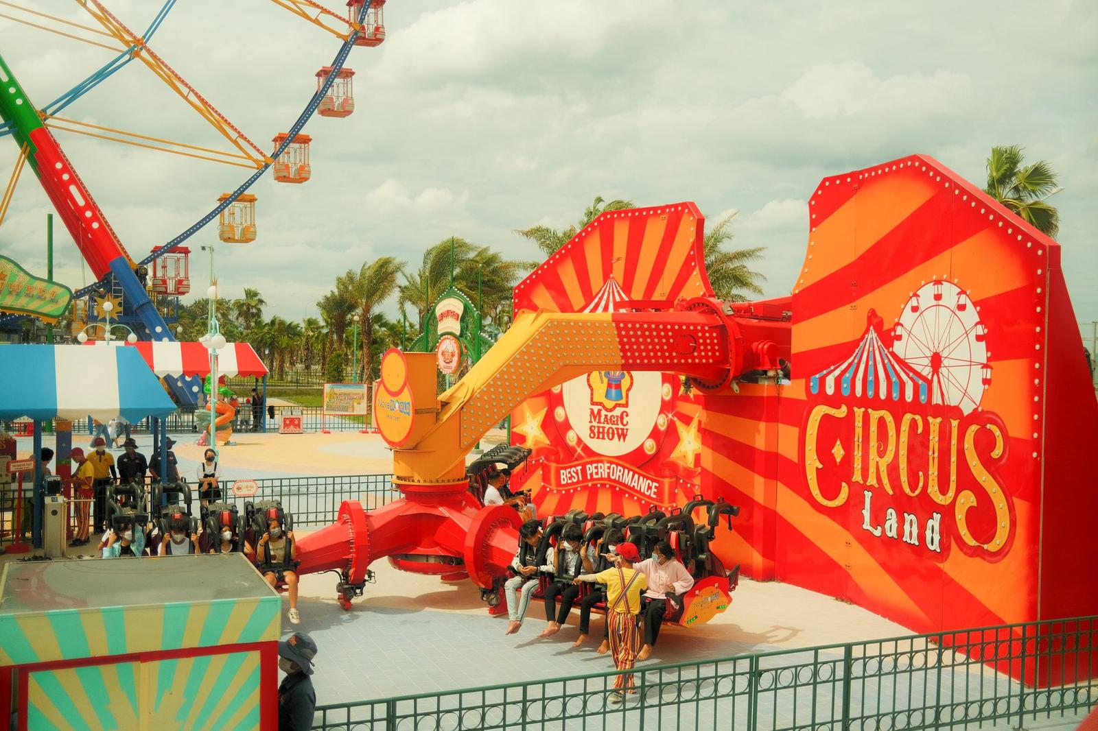 A circus-themed amusement ride with riders in a red and orange car