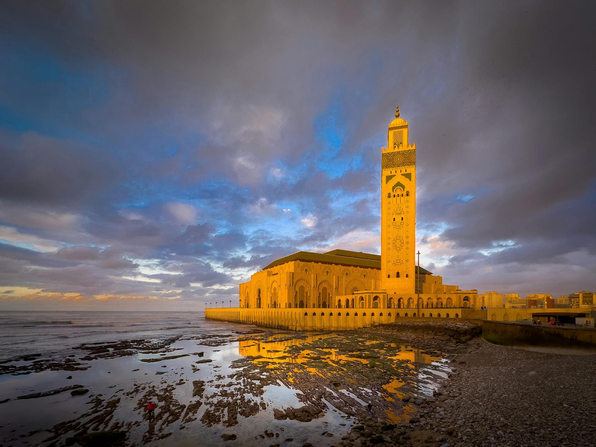 A tall mosque minaret glowing at dusk beside the sea