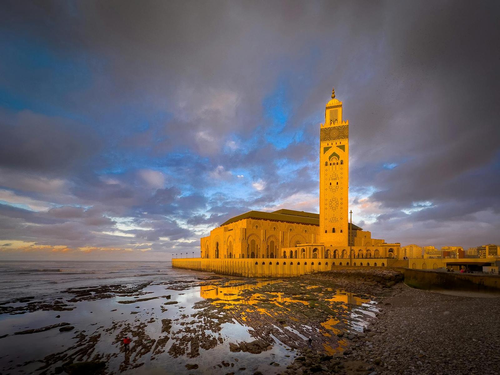 A tall mosque minaret glowing at dusk beside the sea