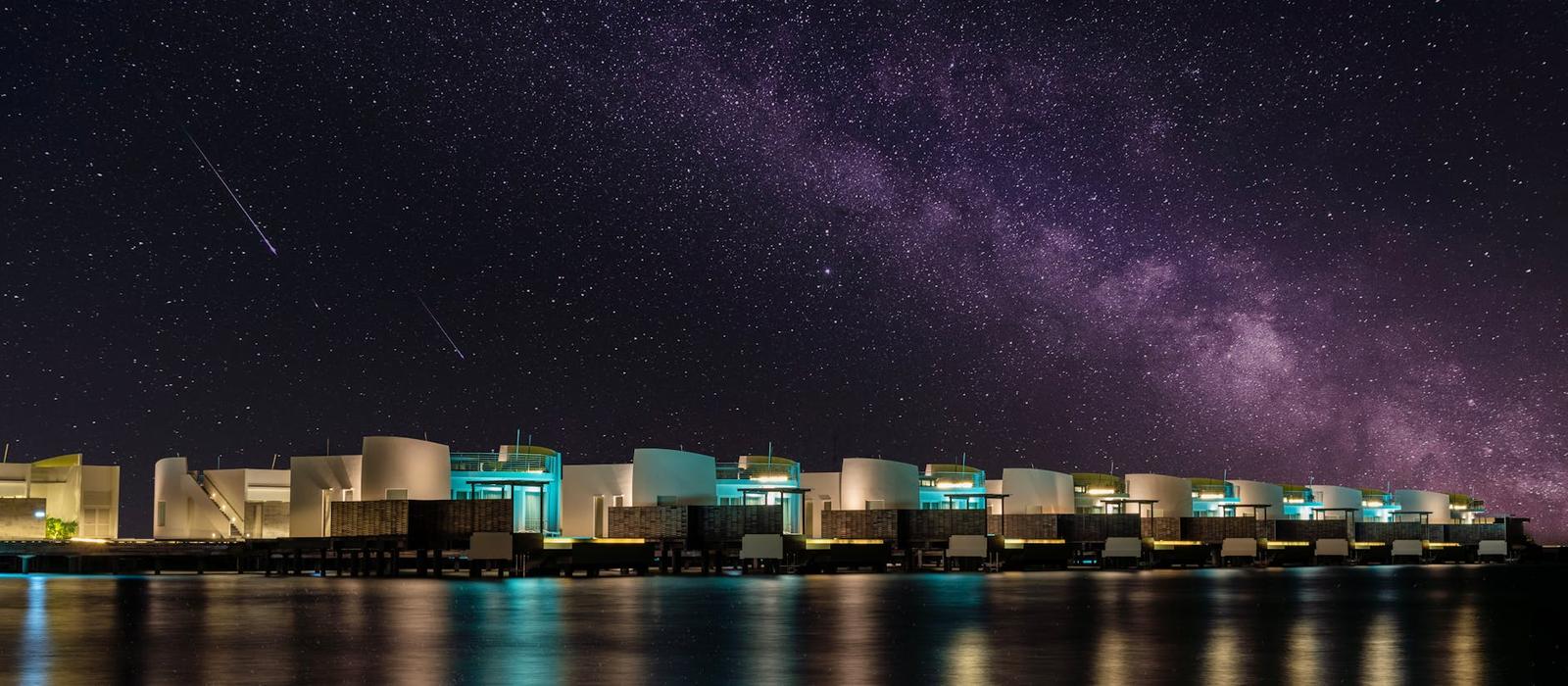 Overwater villas under a starry sky streaked with the Milky Way