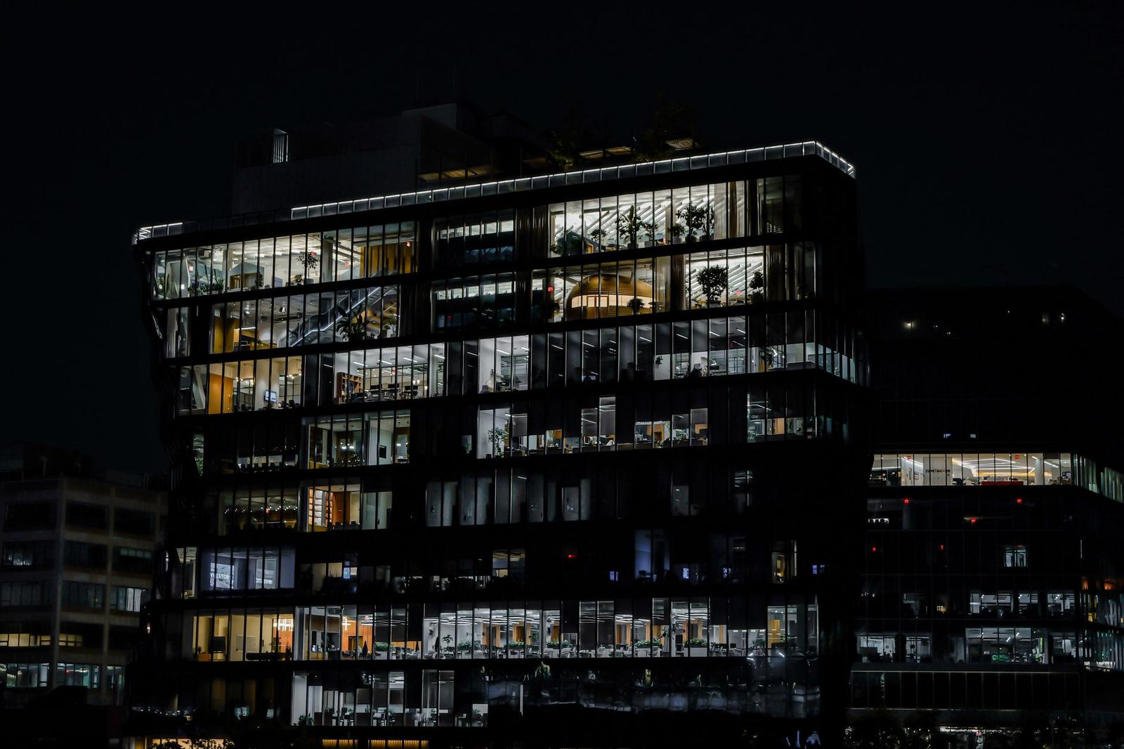 A glass-fronted modern office building lit from within against a dark night sky