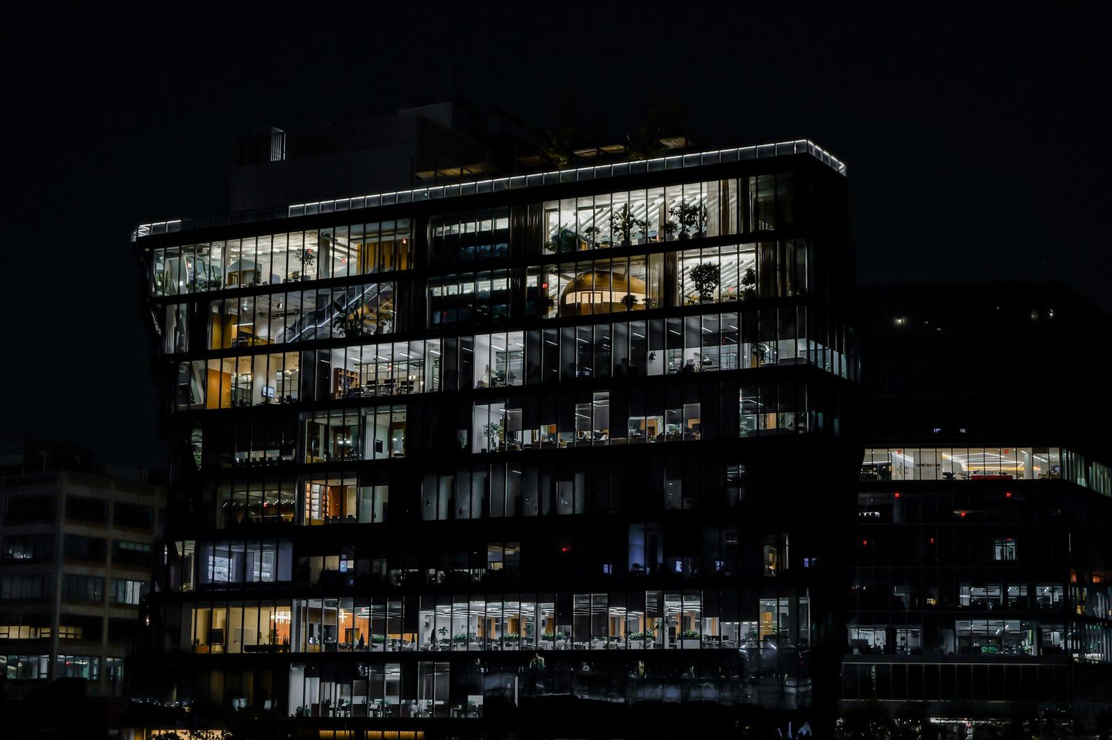A glass-fronted modern office building lit from within against a dark night sky