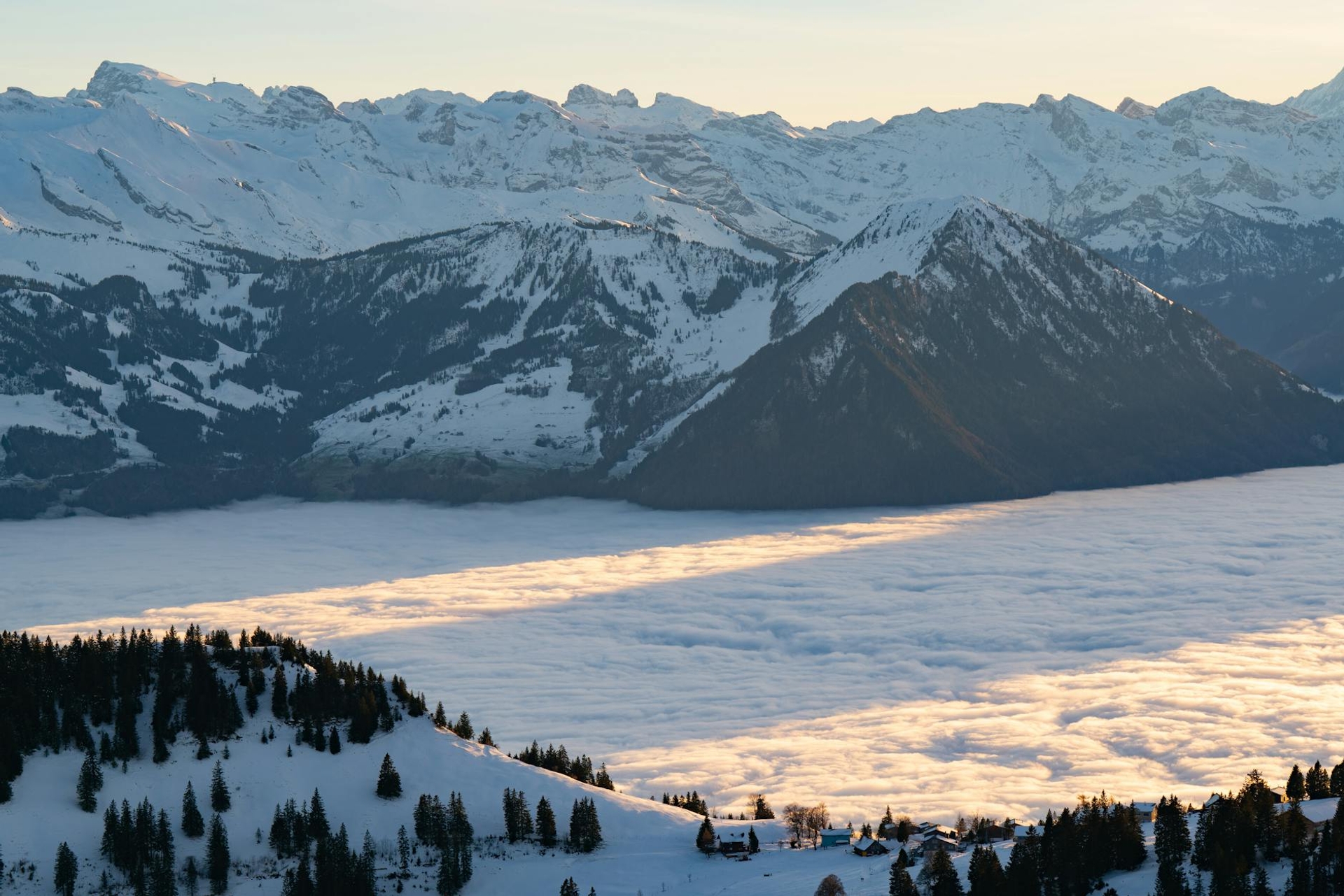 A sea of clouds filling a valley between snow-capped peaks at sunset
