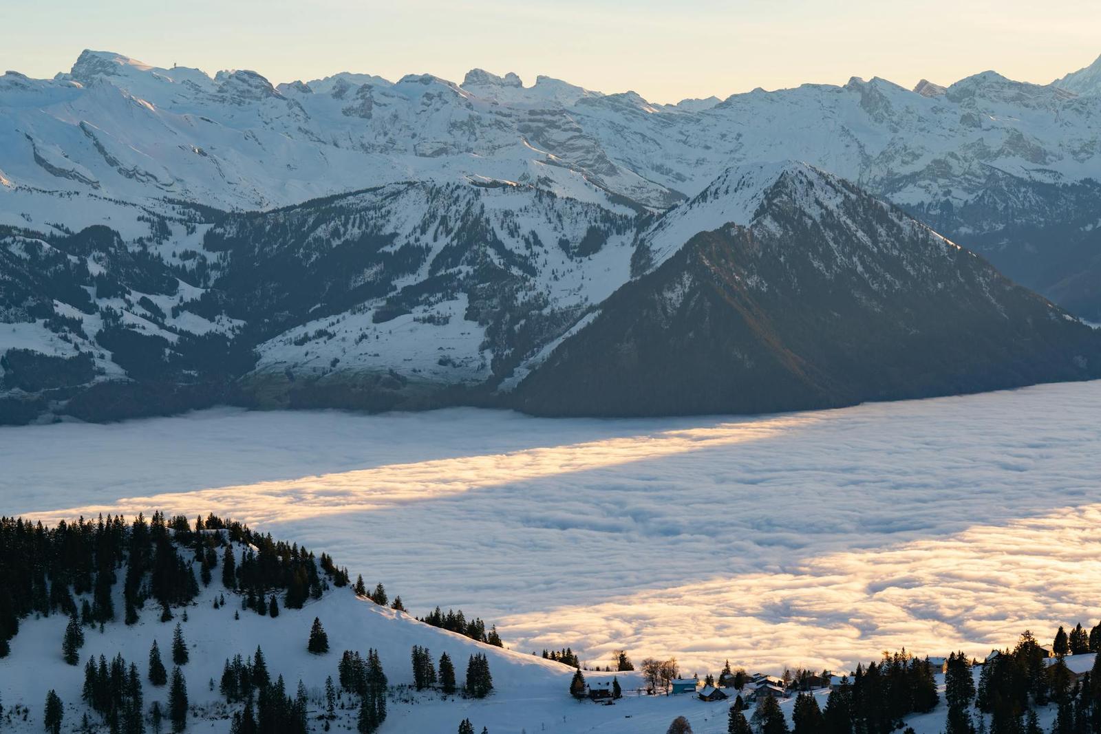 A sea of clouds filling a valley between snow-capped peaks at sunset