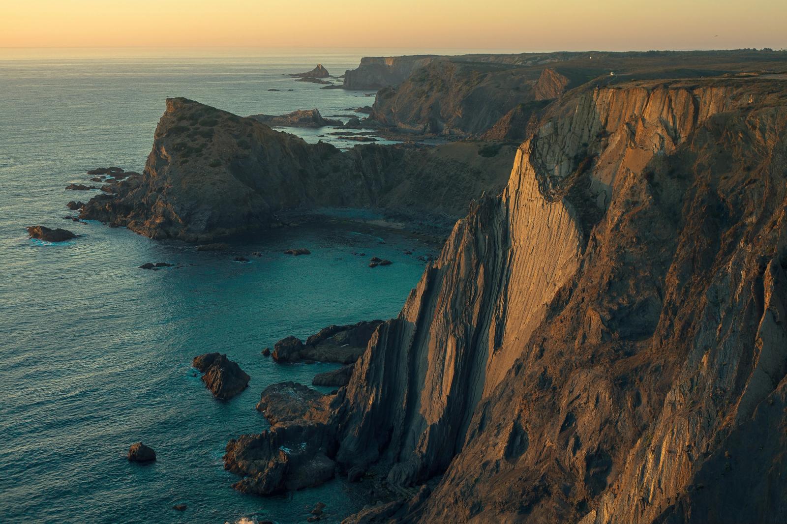 Sunlit sea cliffs dropping into turquoise water along a rugged coastline