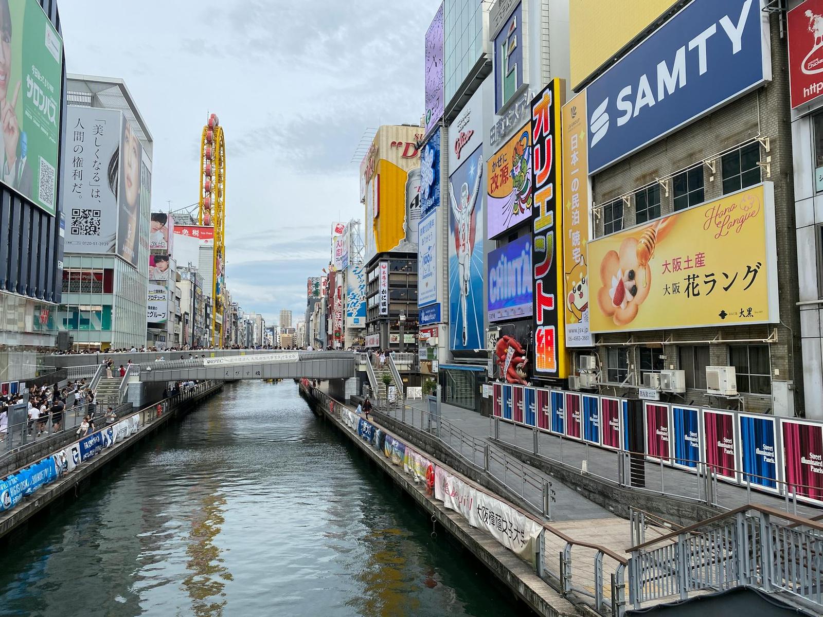 City canal flanked by colourful neon shopfront signs and a footbridge