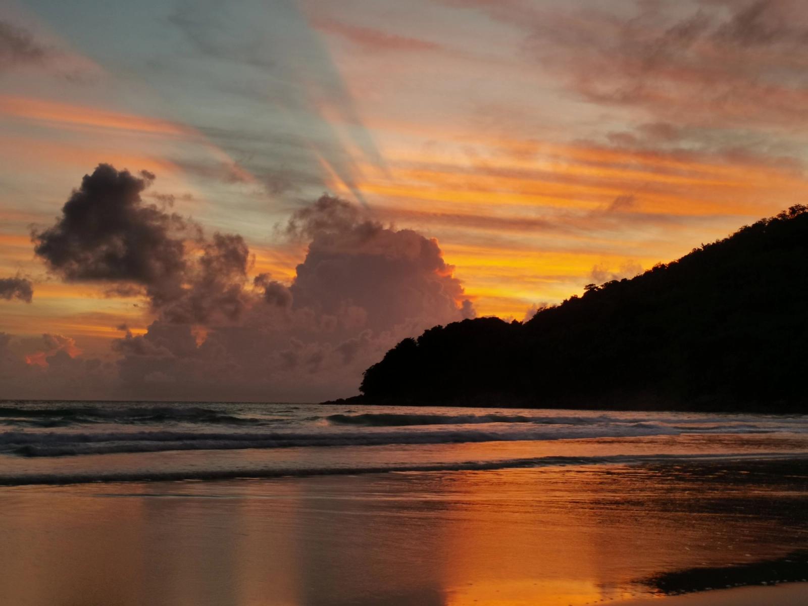 Breathtaking sunset over a serene beach in Phuket with vibrant clouds and calm sea
