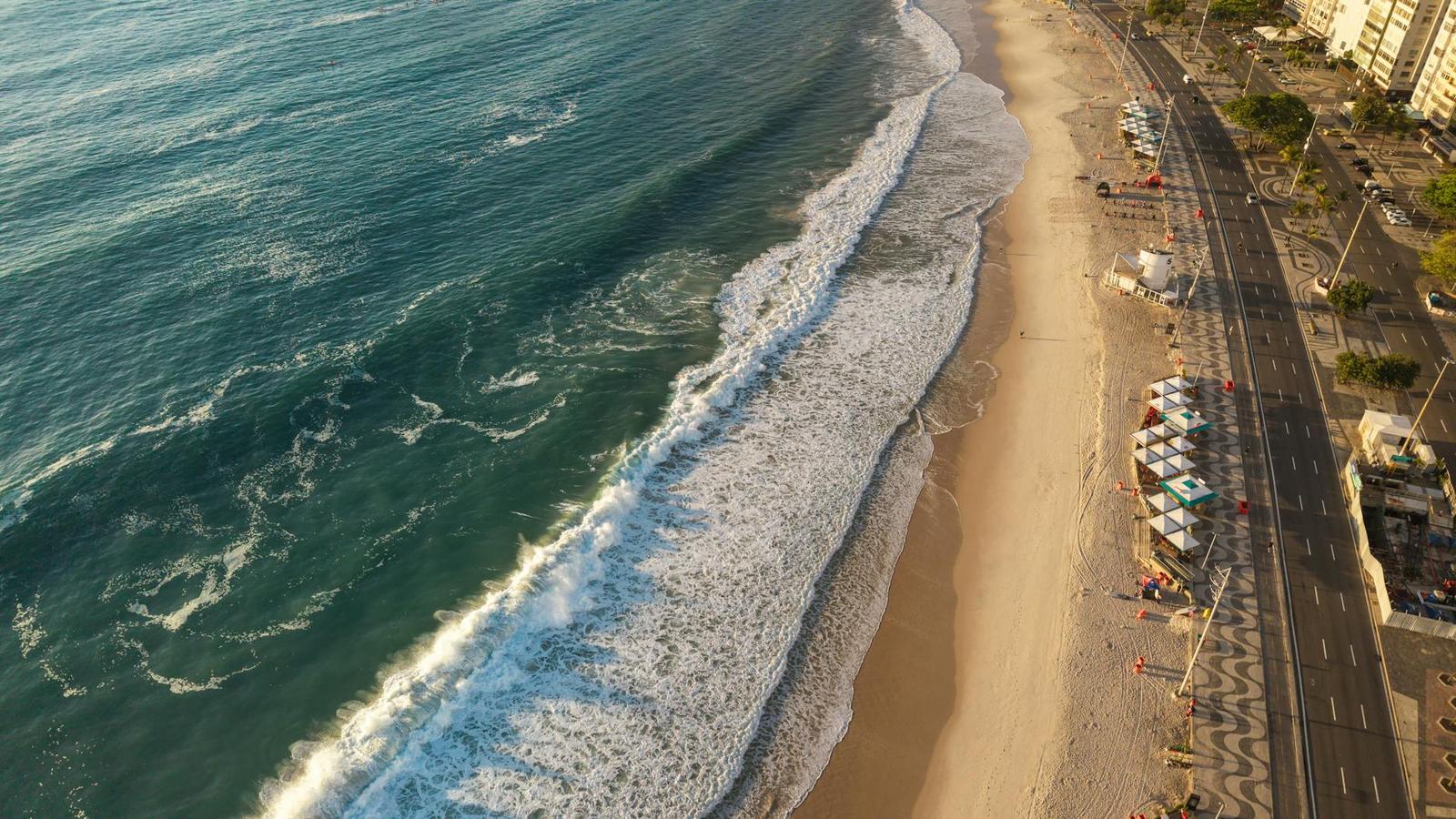 Aerial view of turquoise waves breaking along a sandy beach promenade