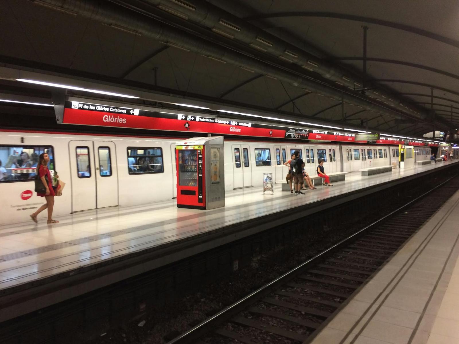 Underground metro platform with a red and white train and a few waiting passengers
