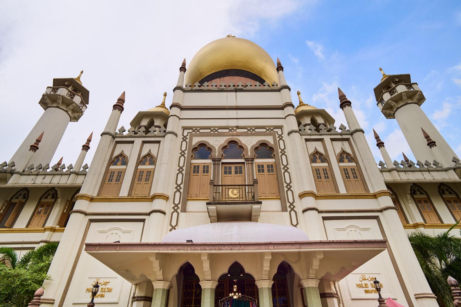 Golden-domed mosque with ornate white minarets against a blue sky