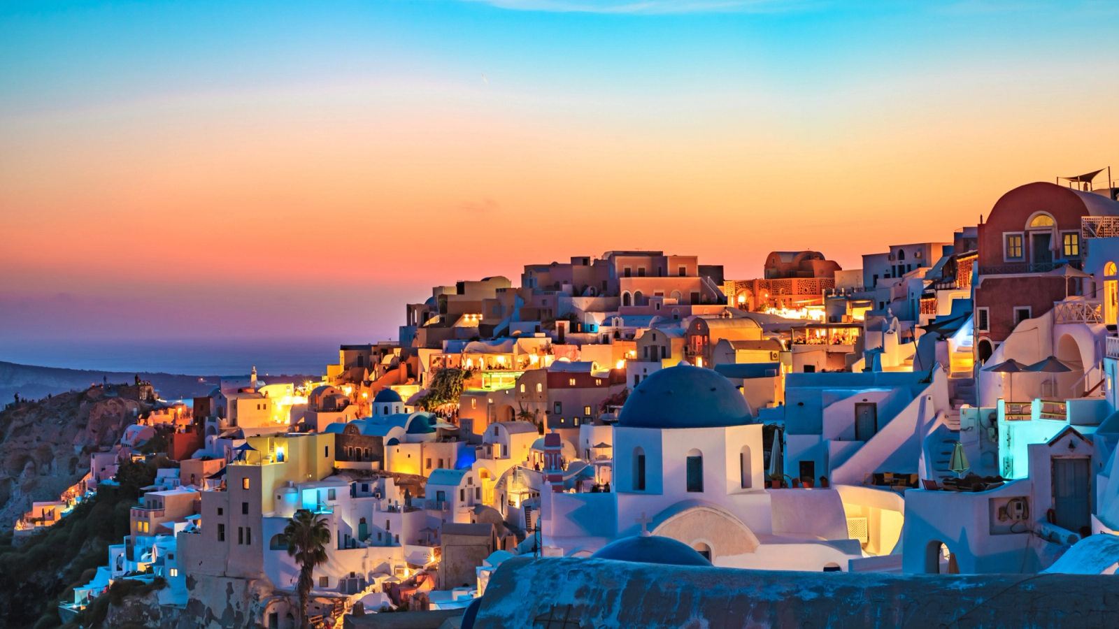 A whitewashed clifftop town with blue-domed churches glowing at sunset
