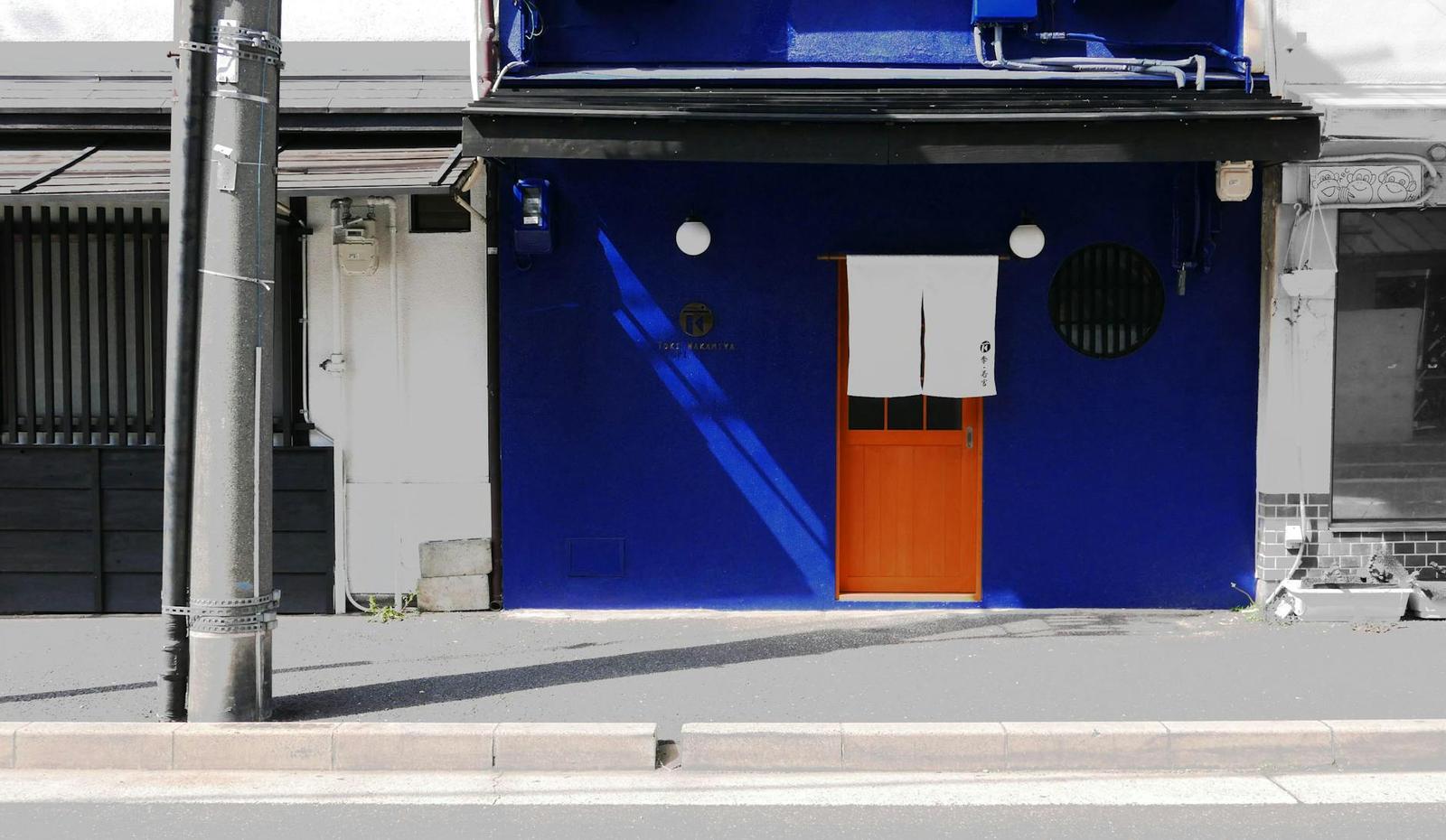 A cobalt blue shopfront with an orange door on a quiet street
