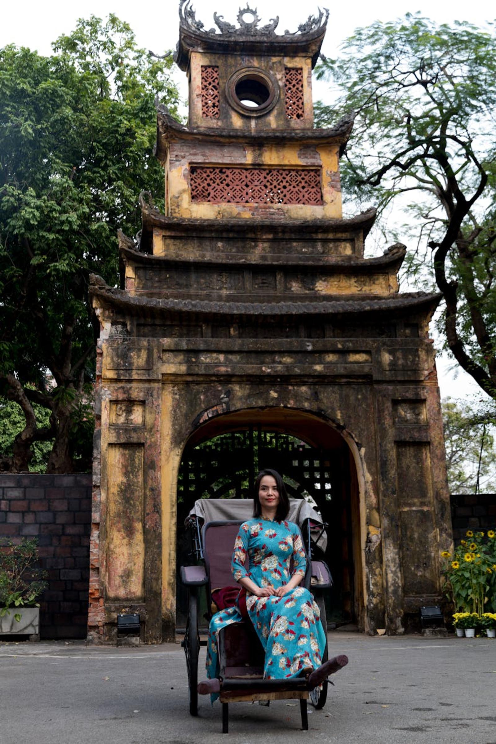 Woman in traditional attire sits in front of a historic gate in Vietnam, exuding cultural charm