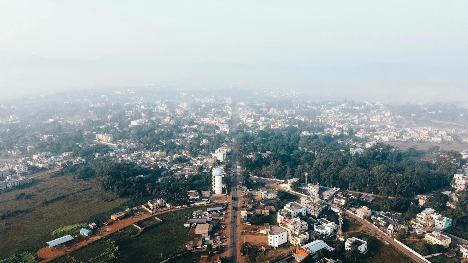 Aerial view of a hazy town spread along a straight road through greenery
