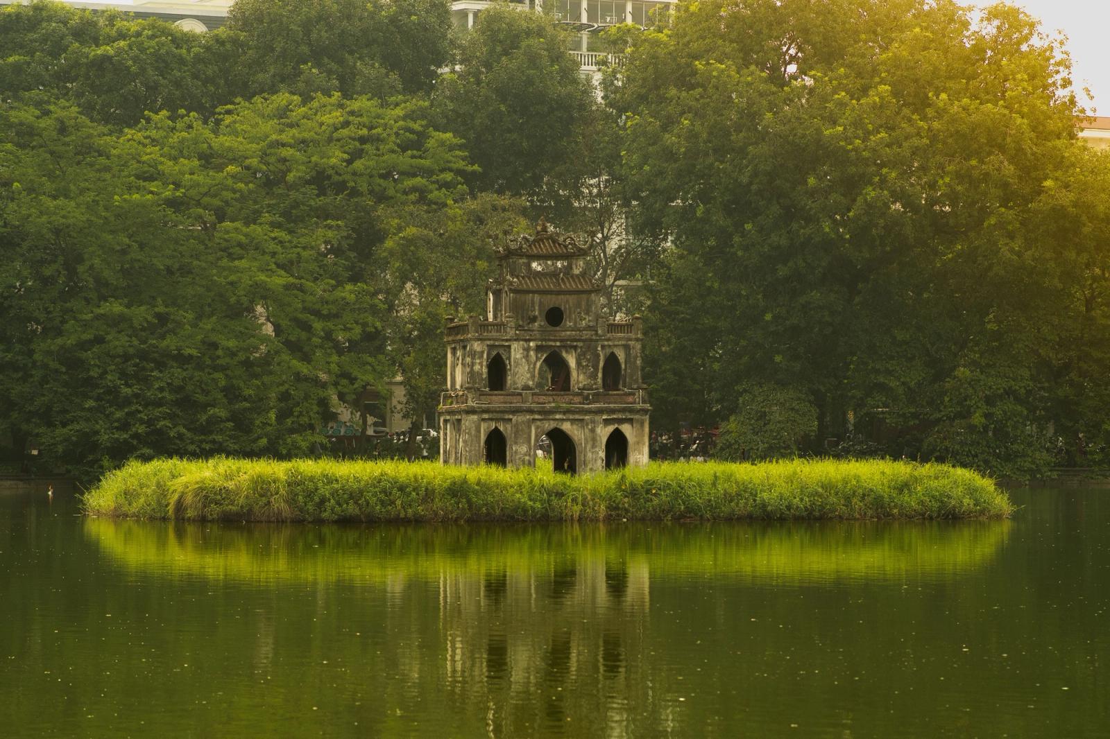 Serene view of Turtle Tower in Hanoi's Hoan Kiem Lake surrounded by lush greenery