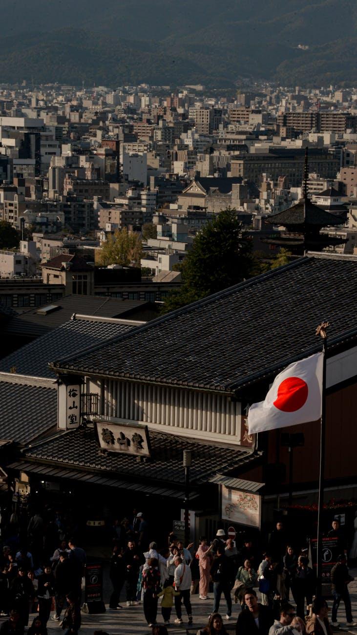 Pagoda tower rising above tiled rooftops with a crowd gathered below a flag