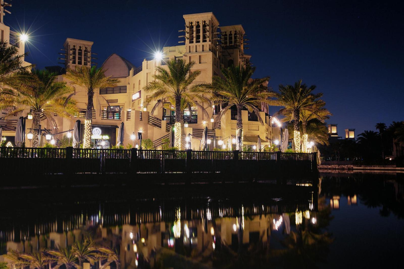 Wind-tower architecture and palm trees reflected in a still canal at night