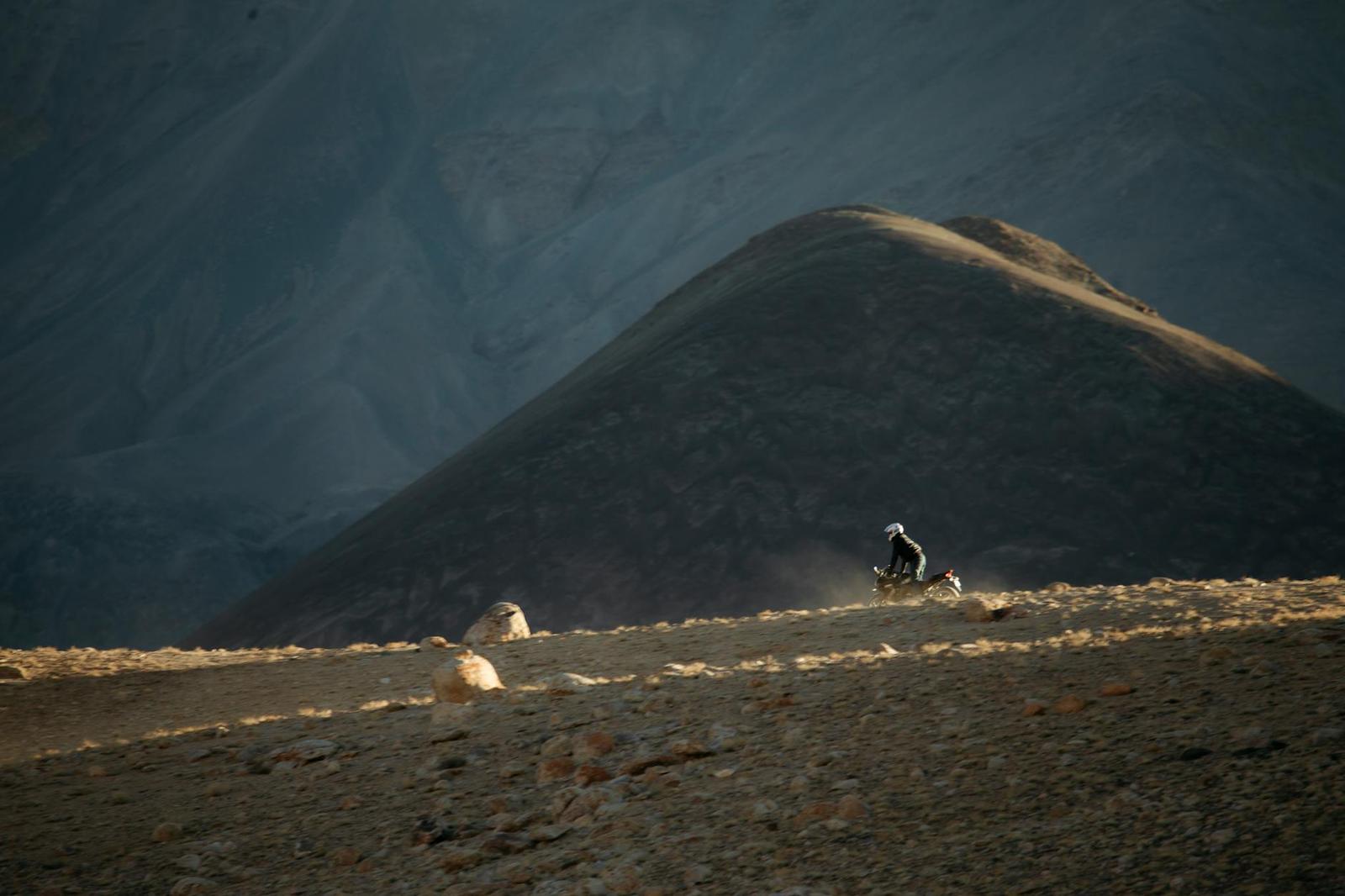 Motorbike rider kicking up dust on a high desert track between barren hills