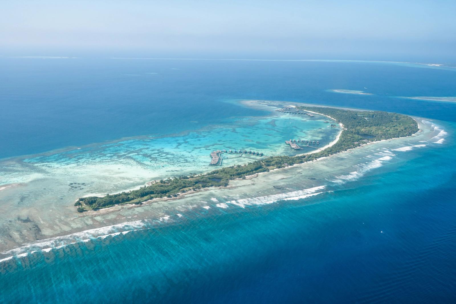 Aerial view of a reef-fringed resort island tapering into the sea