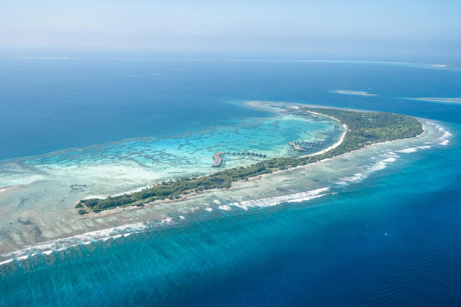 Aerial view of a reef-fringed resort island tapering into the sea