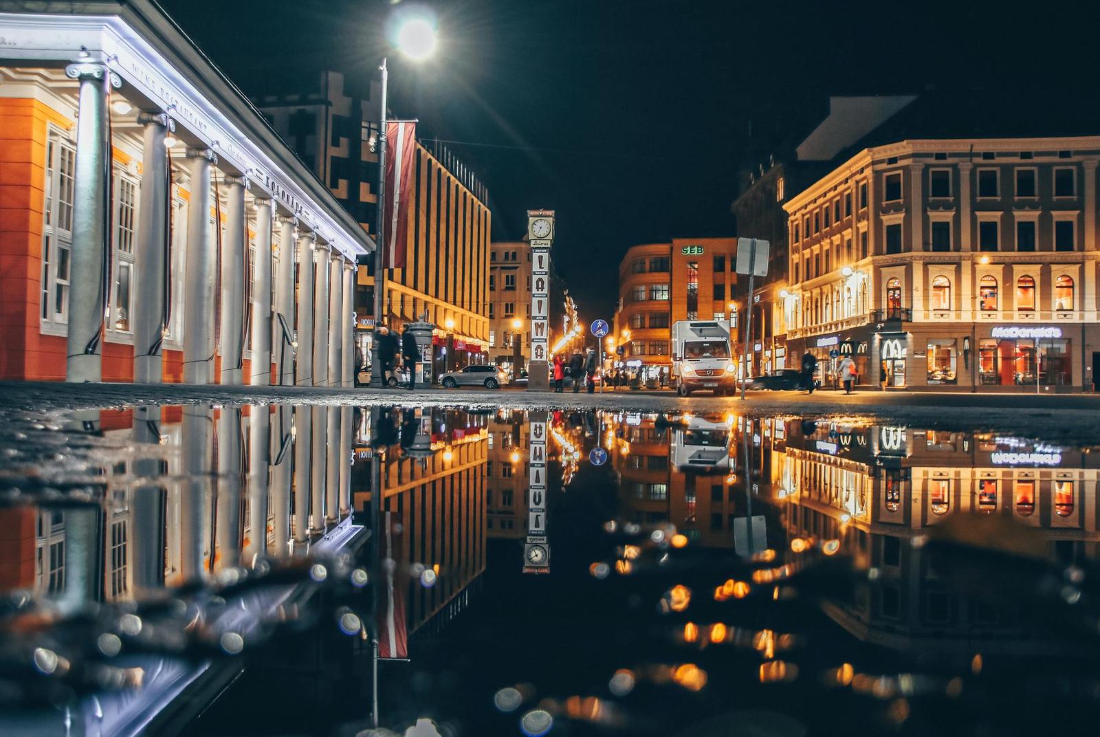 A lit city street reflected in wet pavement at night