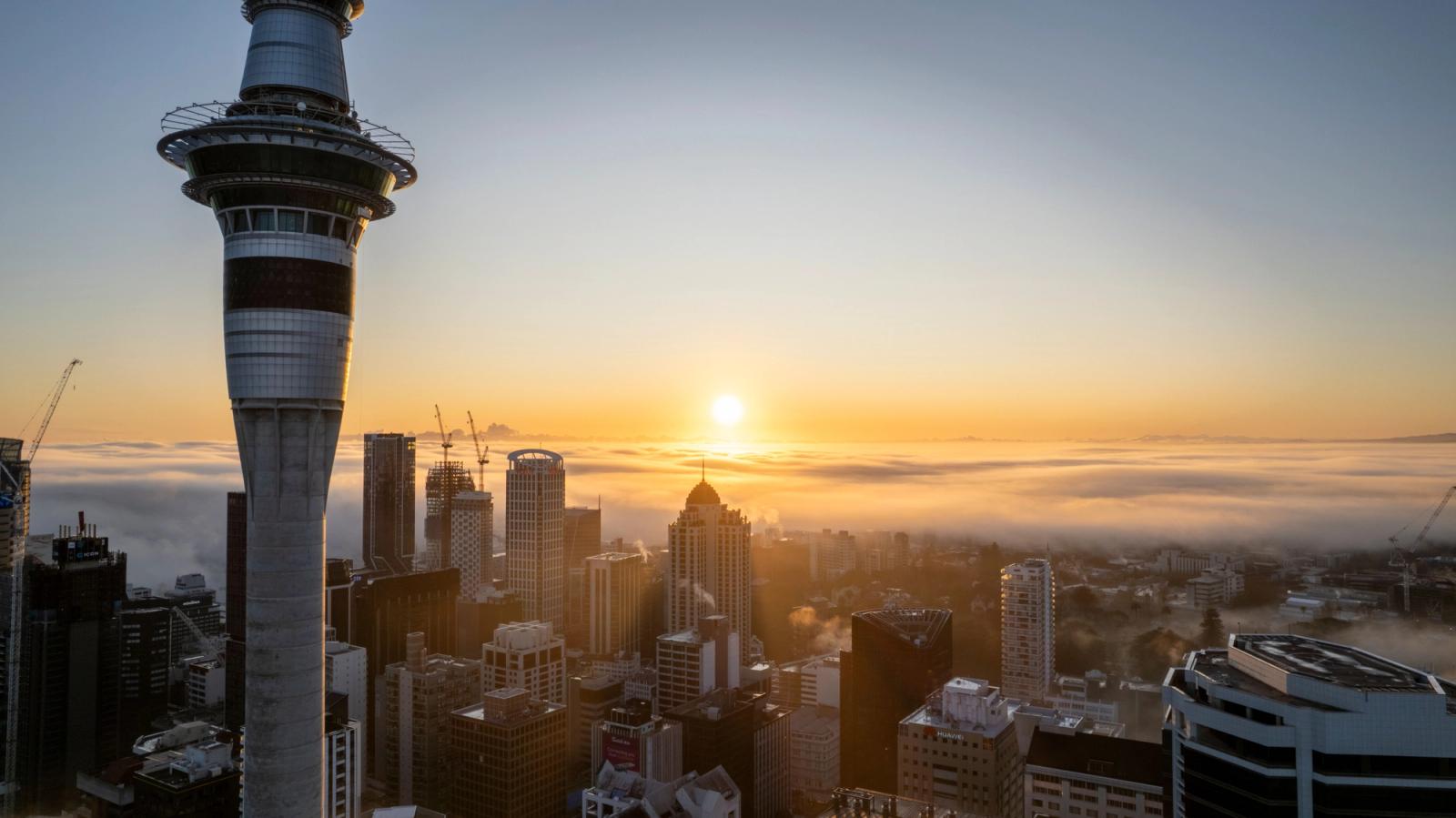 Breathtaking sunrise over Auckland cityscape featuring the iconic Sky Tower amidst fog