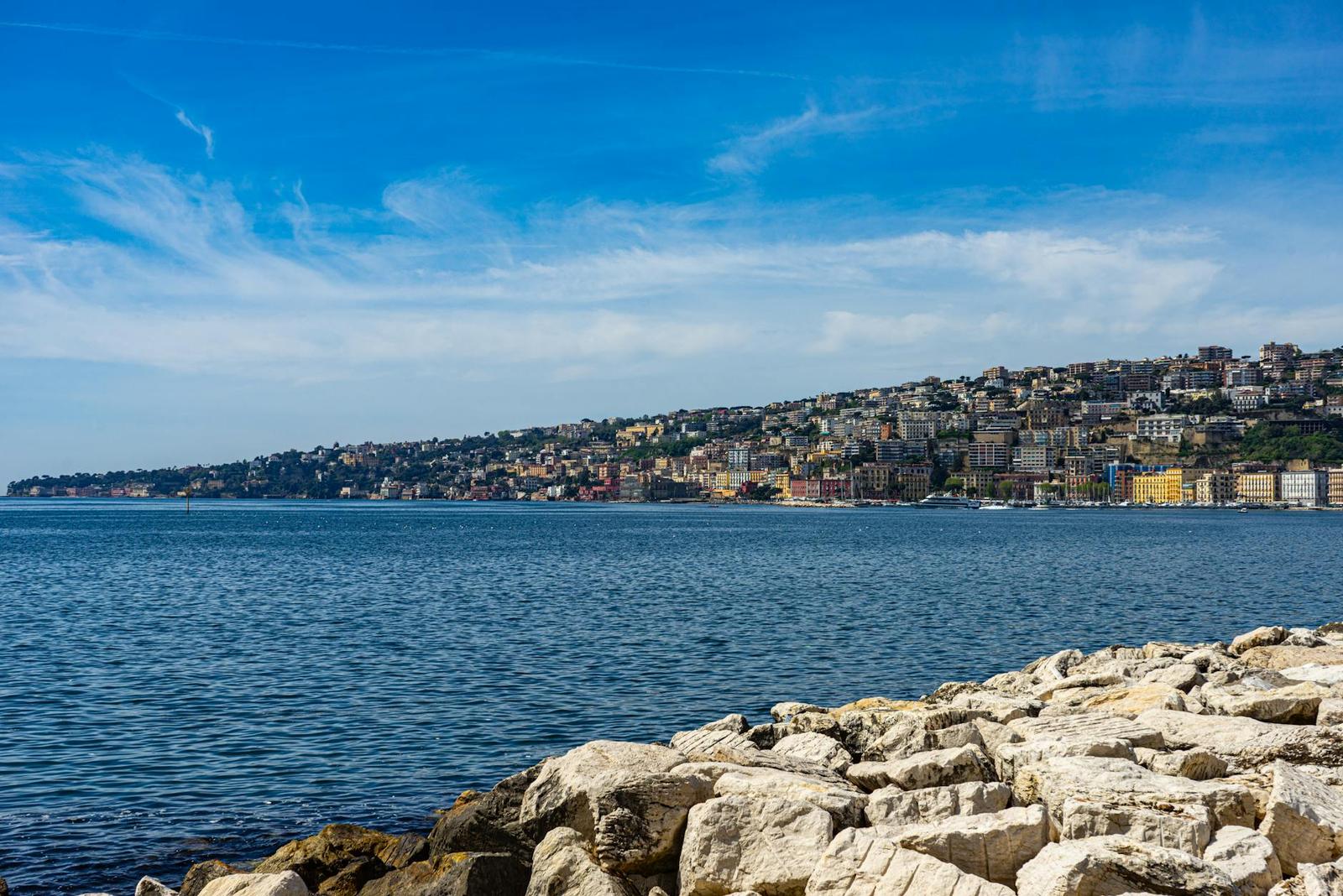 Rocky shoreline looking across calm water toward a hillside coastal town