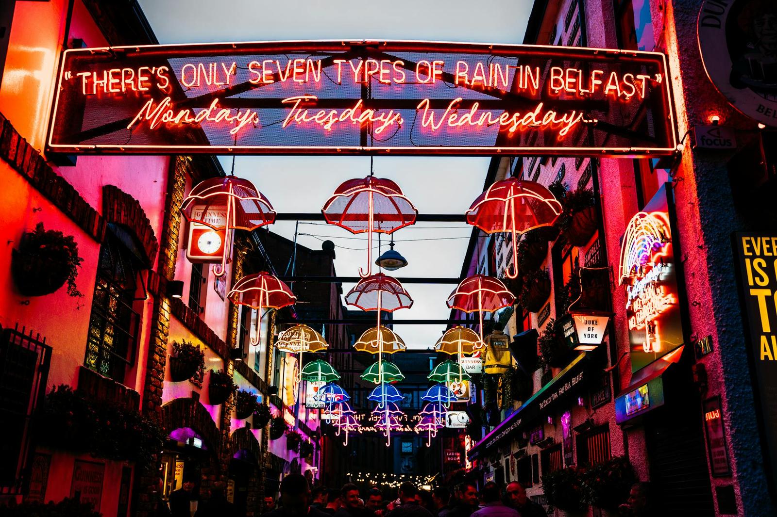 Colourful umbrellas and neon signage strung above a bustling pub alley at night