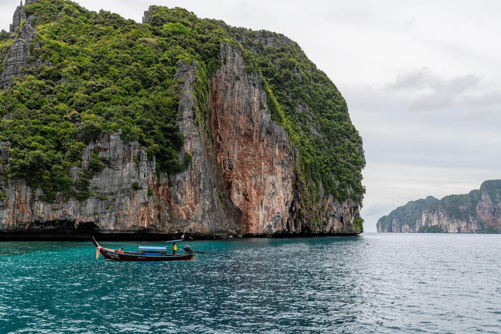 A longtail boat navigating the stunning limestone cliffs of Phuket, Thailand's vibrant ocean landscape