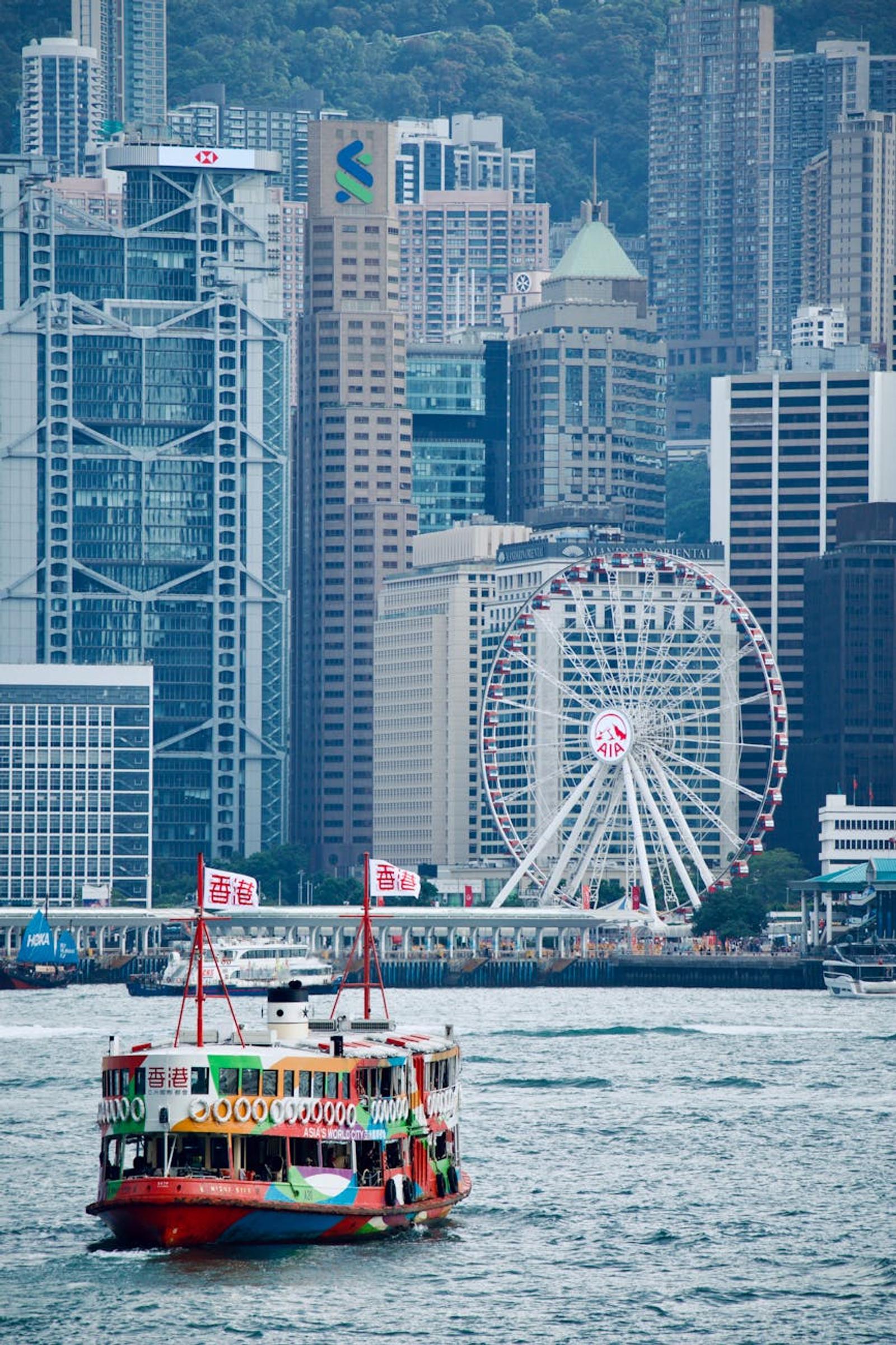 Stunning shot of Hong Kong's skyline featuring a ferry and prominent landmarks like the Ferris Wheel
