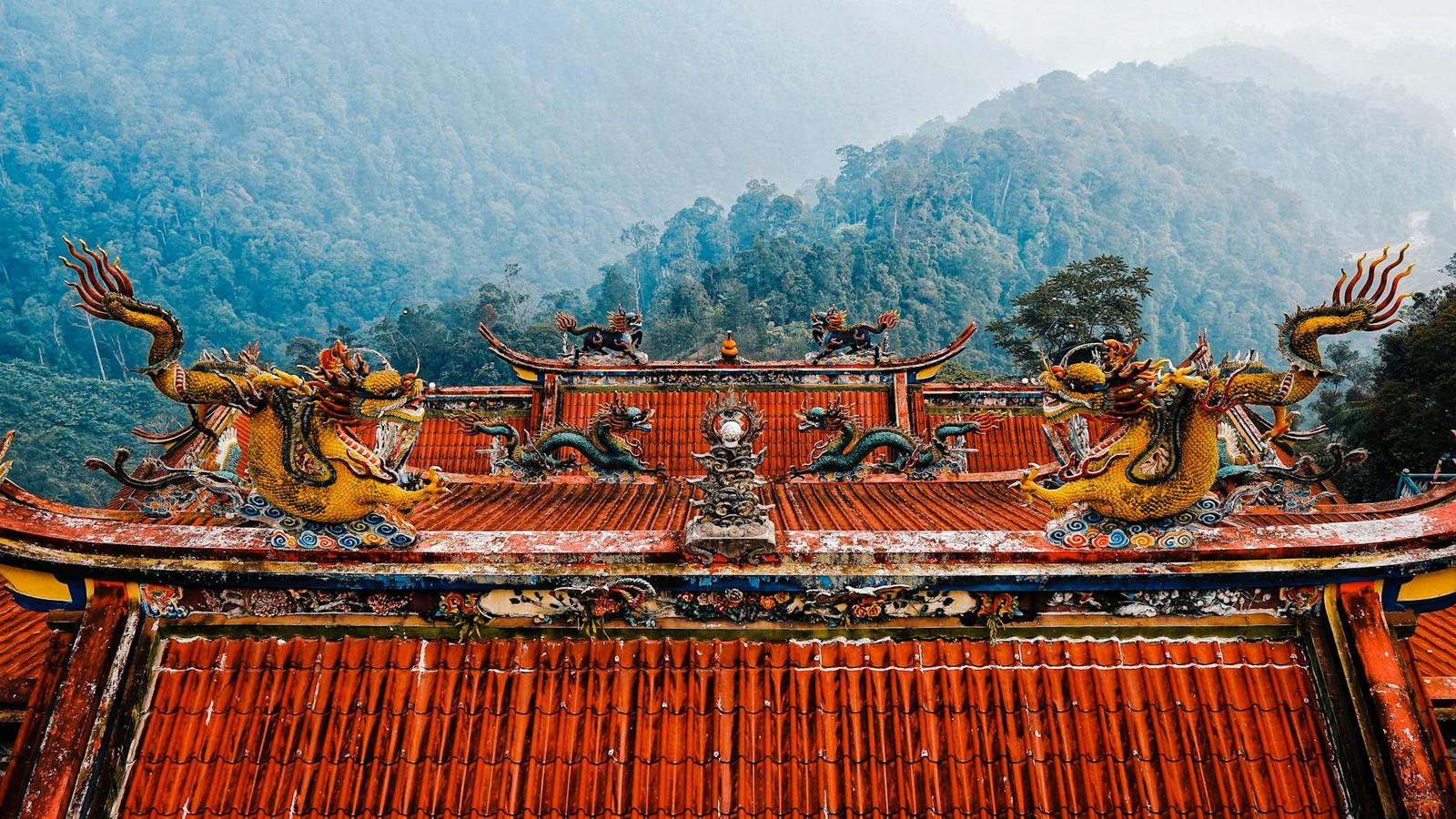Dragon sculptures atop a red-tiled temple roof against misty forested hills