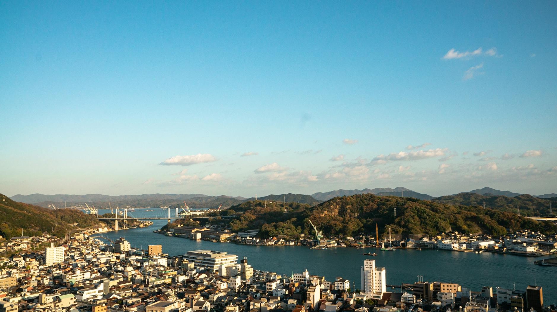 Aerial view of a bay town with a suspension bridge and forested hills