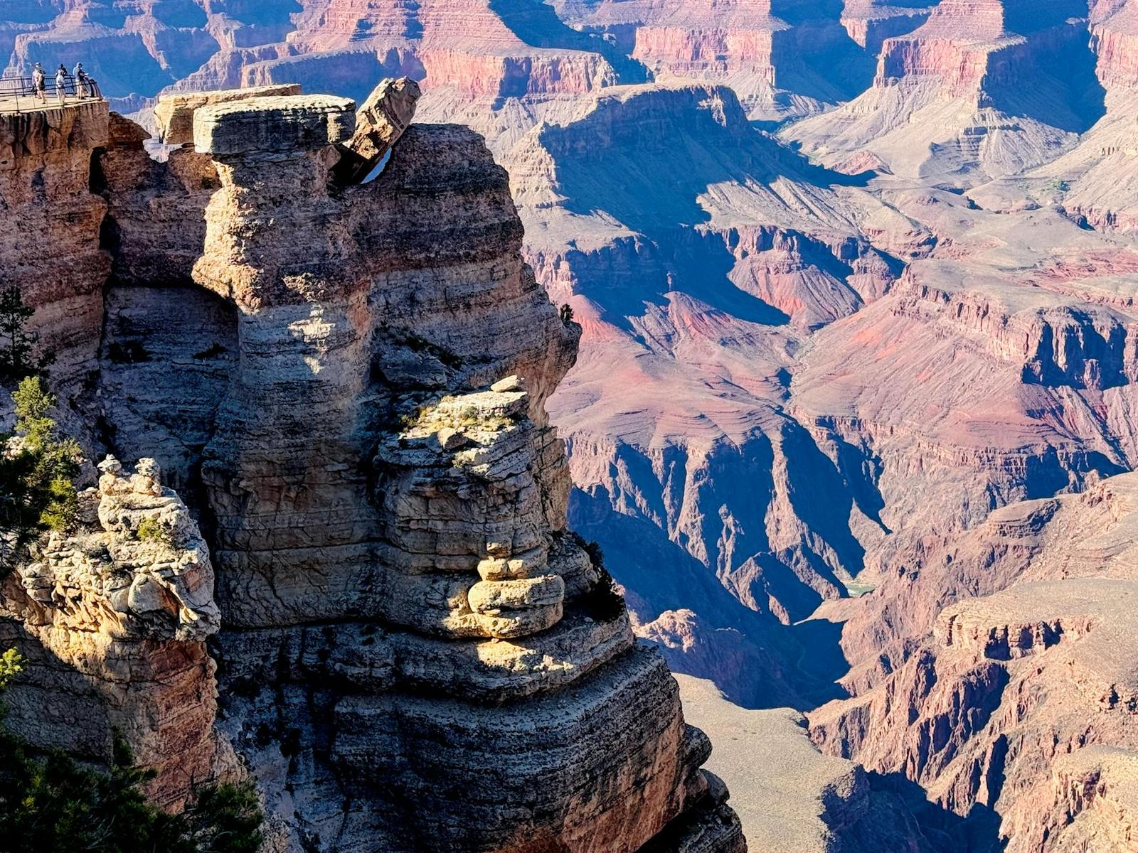 People standing atop a jagged rock spire above a deep layered canyon