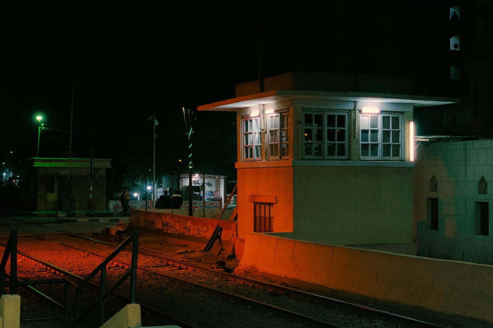 A lit signal box beside railway tracks glowing orange at night
