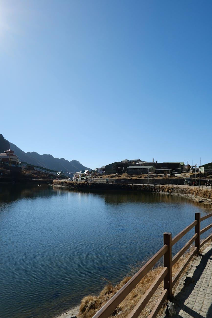 Calm mountain lake framed by a wooden fence and distant village