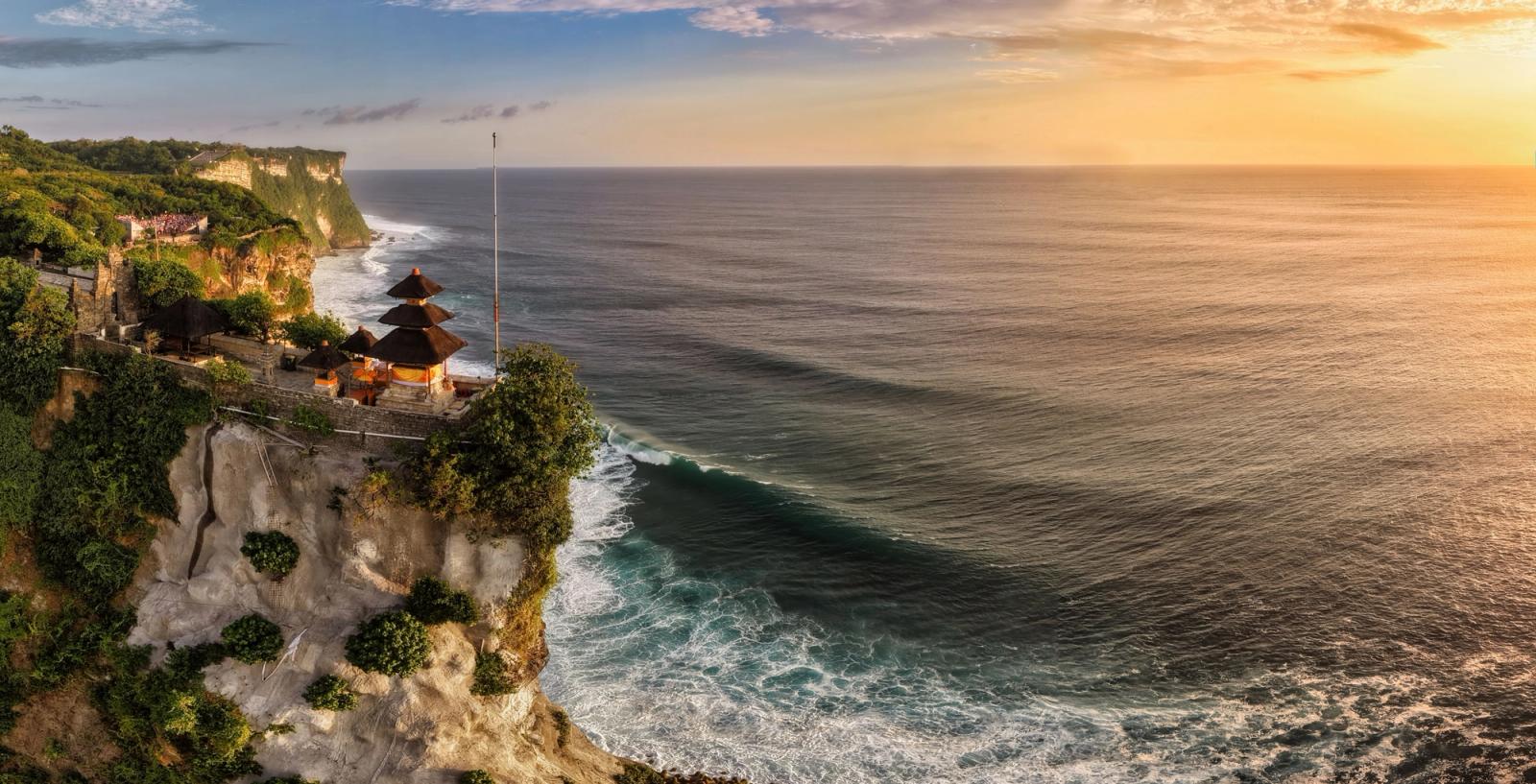 A small temple pavilion perched on a cliff edge above the sea at sunset