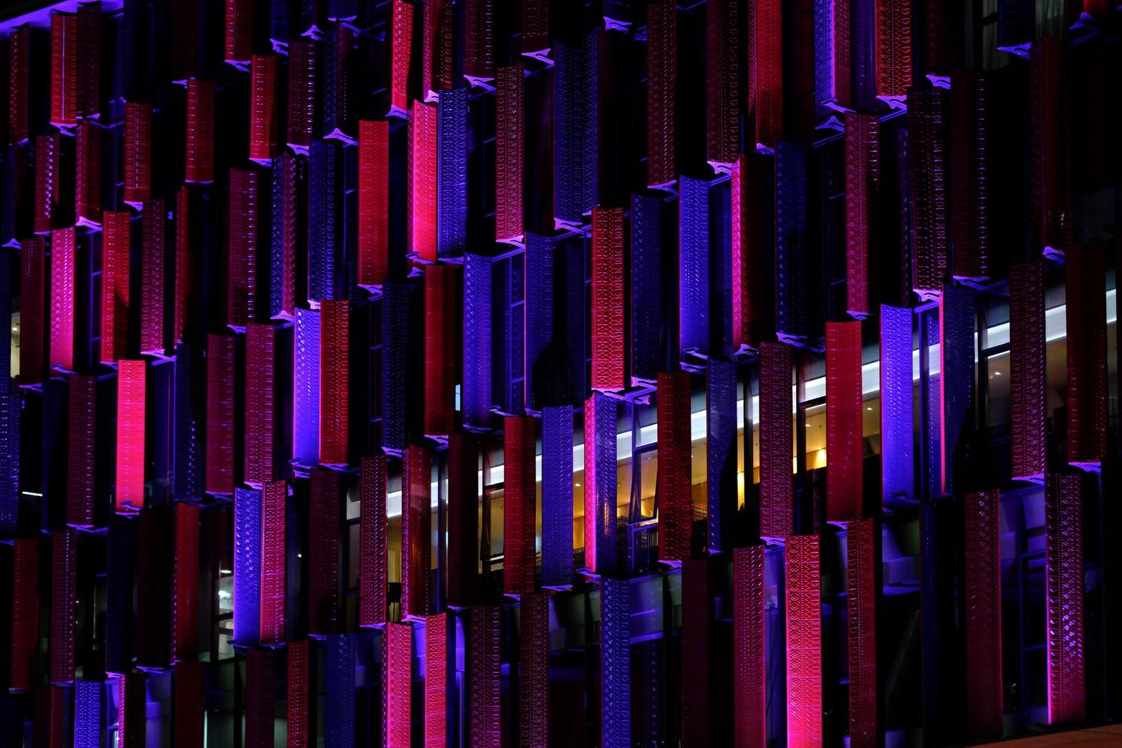 Vertical fins of a building facade lit in red and purple at night