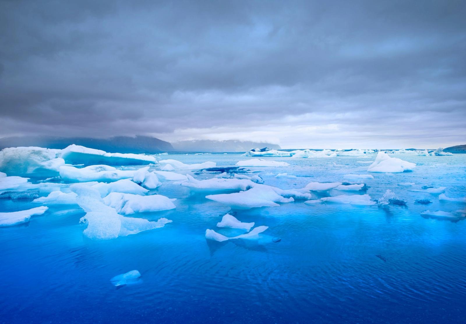 Chunks of blue ice floating in a glacial lagoon under stormy skies