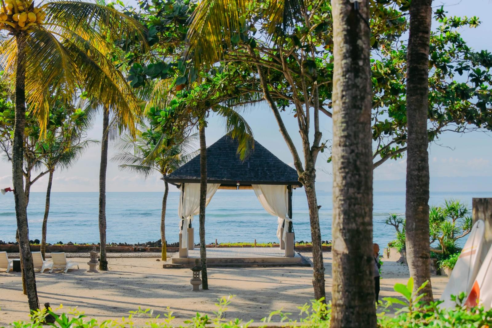 Tropical pavilion with palm trees by the beach in Bali, Indonesia, offering a serene coastal view