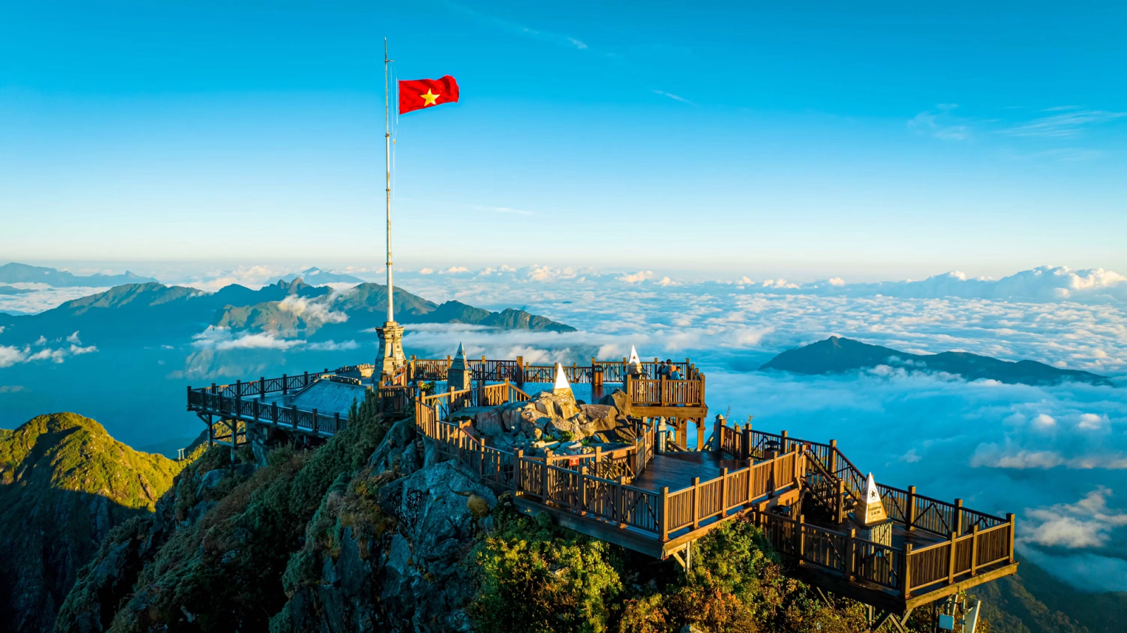A mountaintop viewing platform with a flagpole rising above a sea of clouds