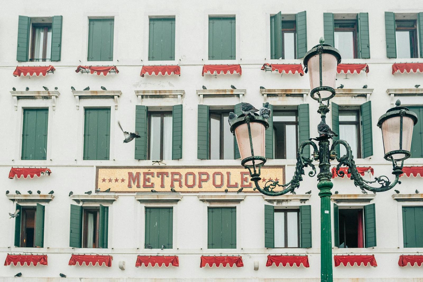 A white hotel facade with green shutters, red awnings and an ornate lamppost