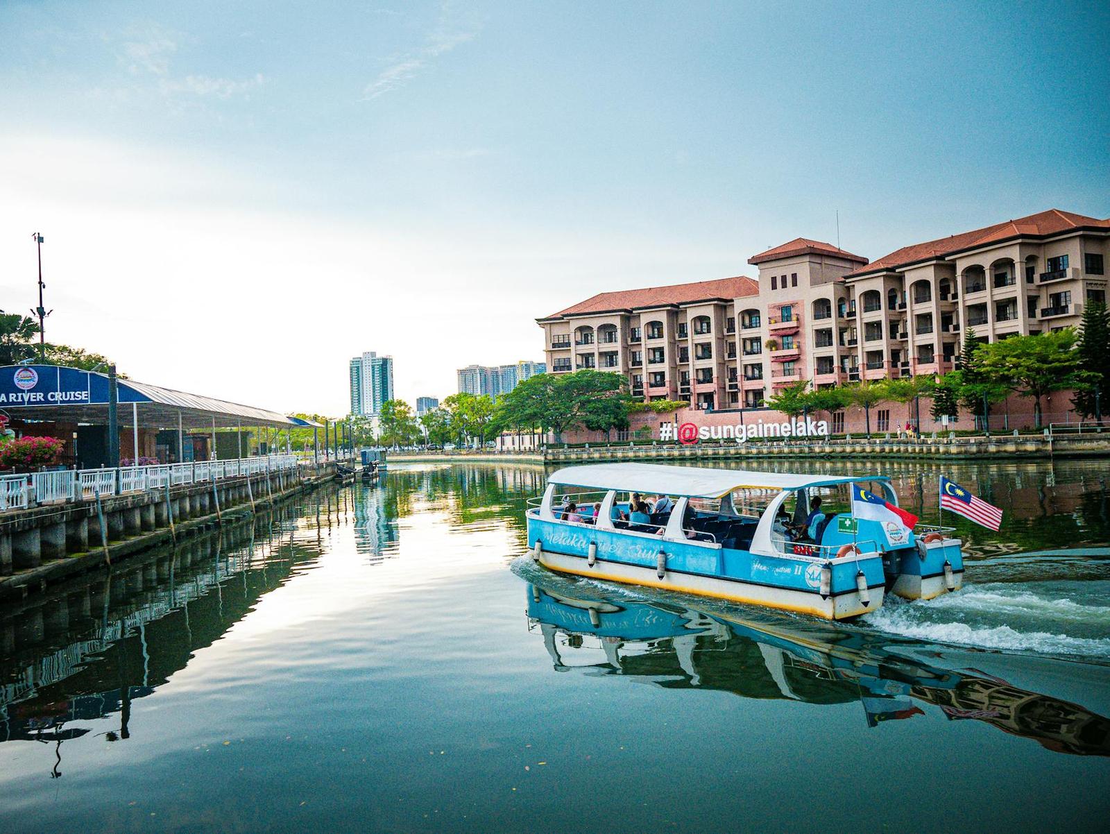 A river cruise boat passing a red-roofed building along a waterway