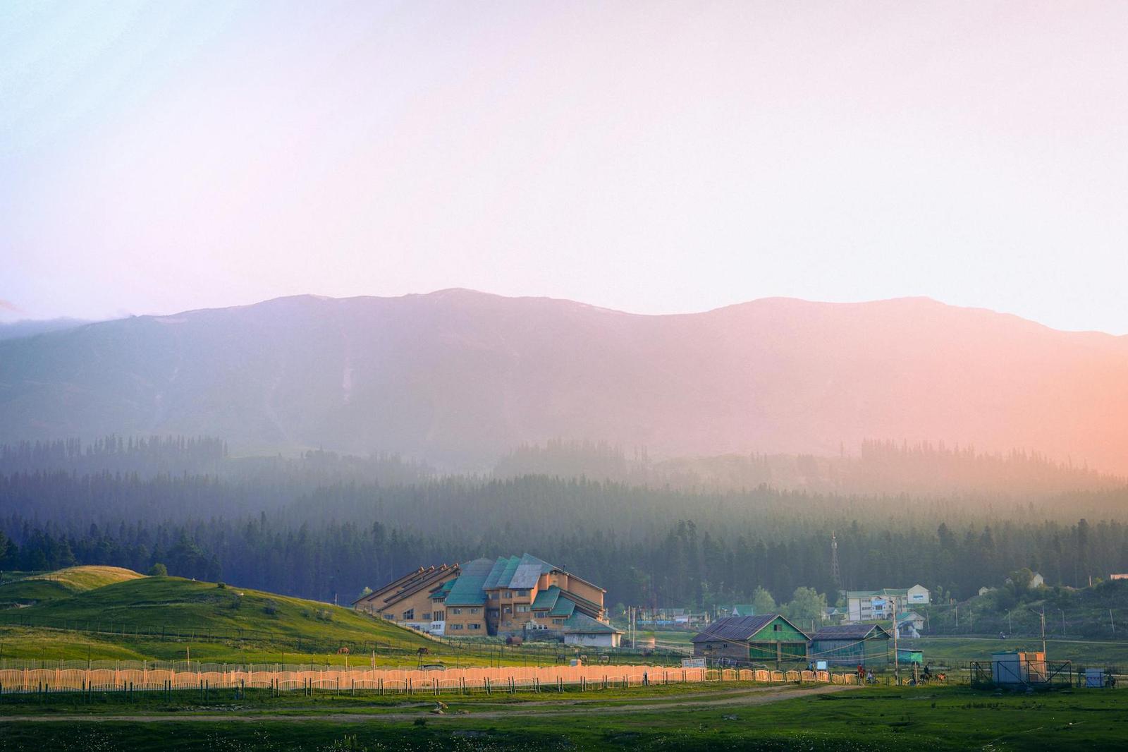 A green valley resort glowing under a hazy sunset behind pine ridges