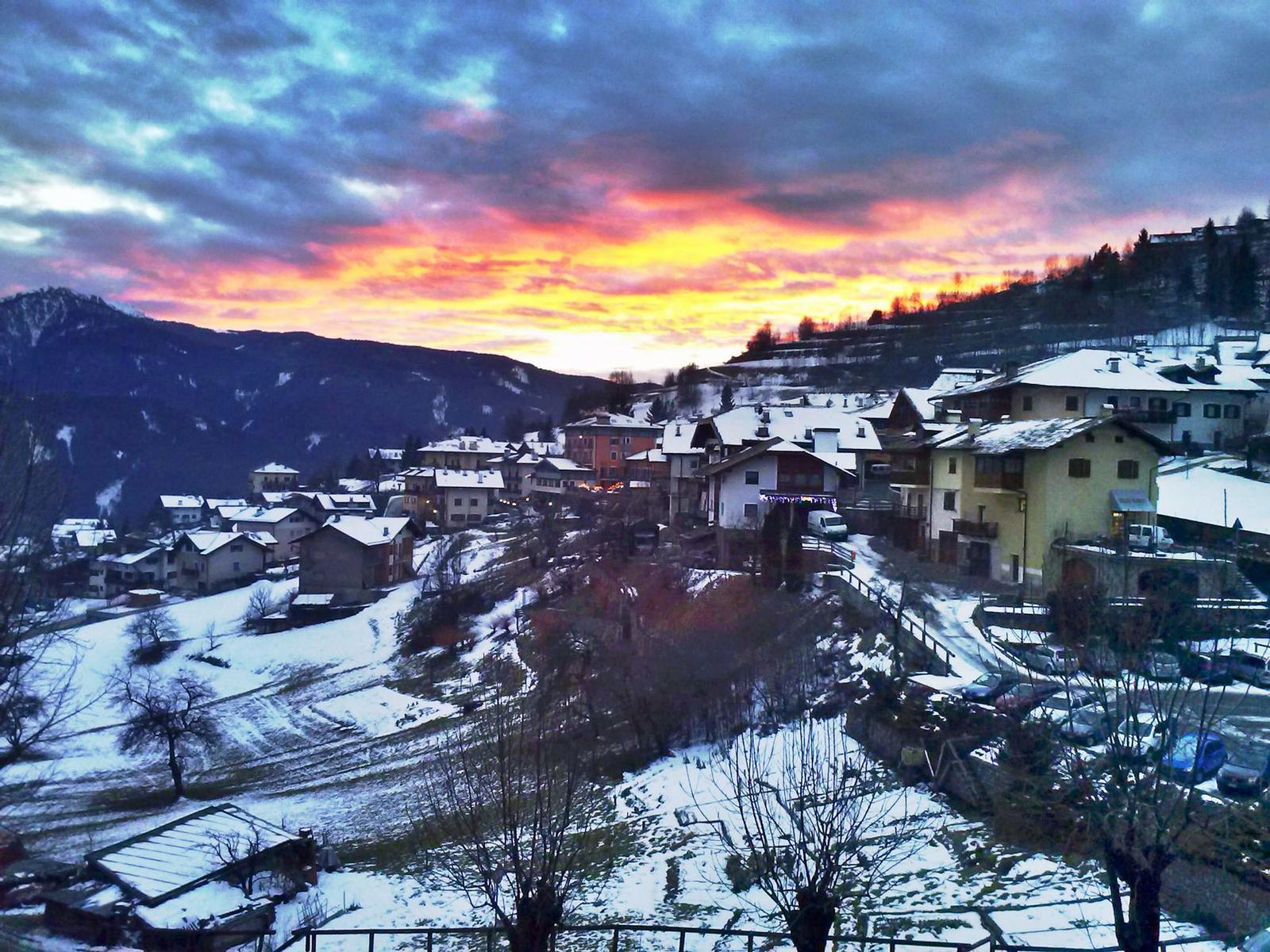 A snow-covered mountain village beneath a fiery orange sunset sky