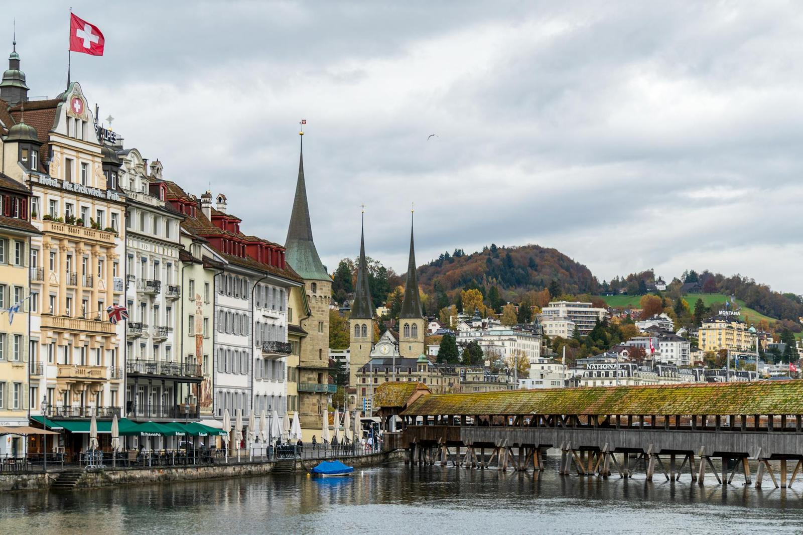 Riverside old town with church spires and a flag-lined promenade beside a wooden bridge