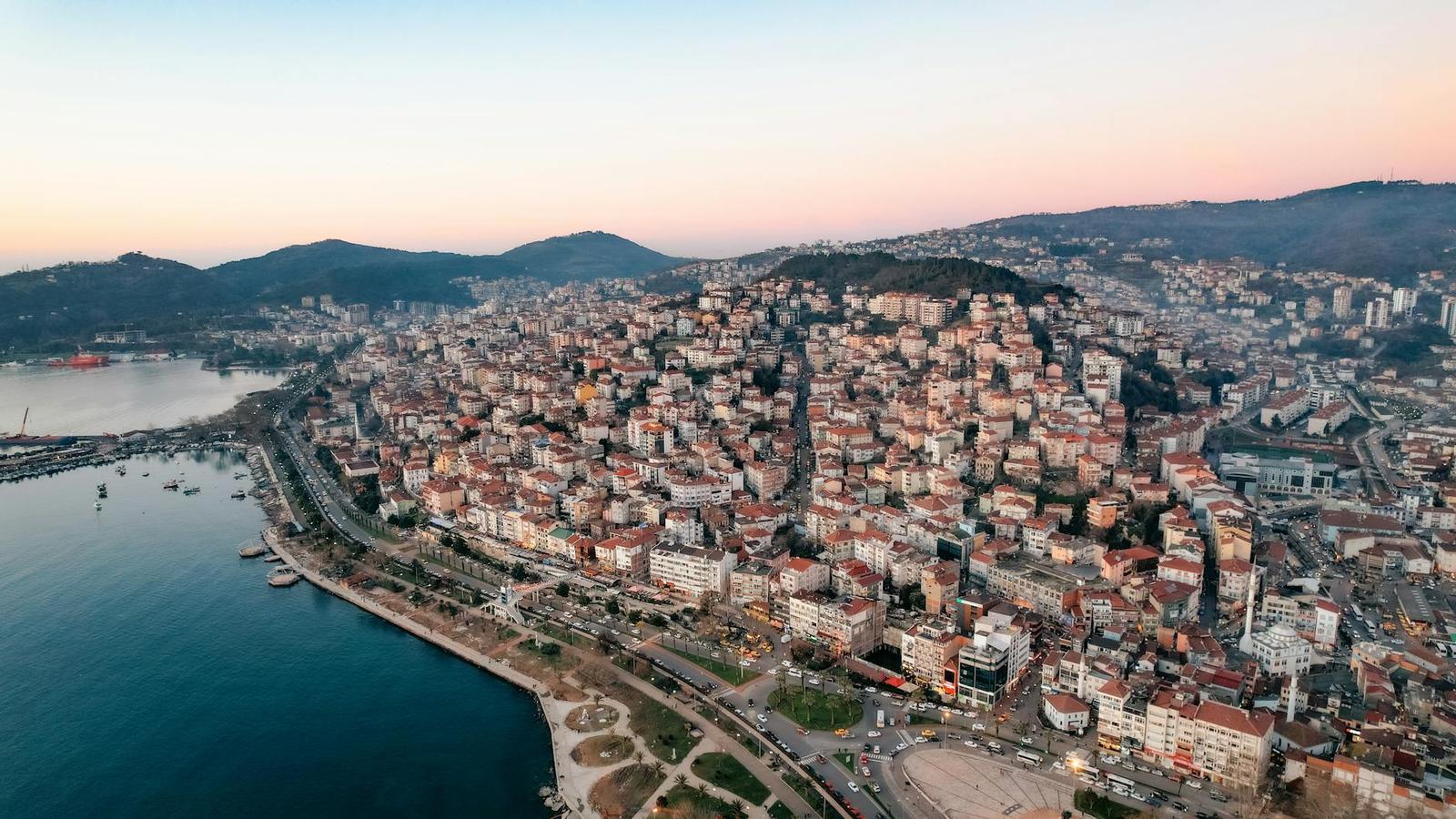 Aerial view of a dense hillside town along a curving coastline at dusk